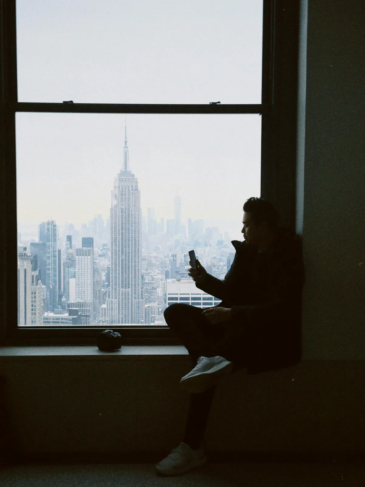 Person using phone while looking out a window at a city skyline