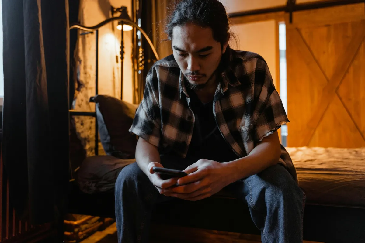 Persona seduta sola che guarda il telefono con espressione pensierosa